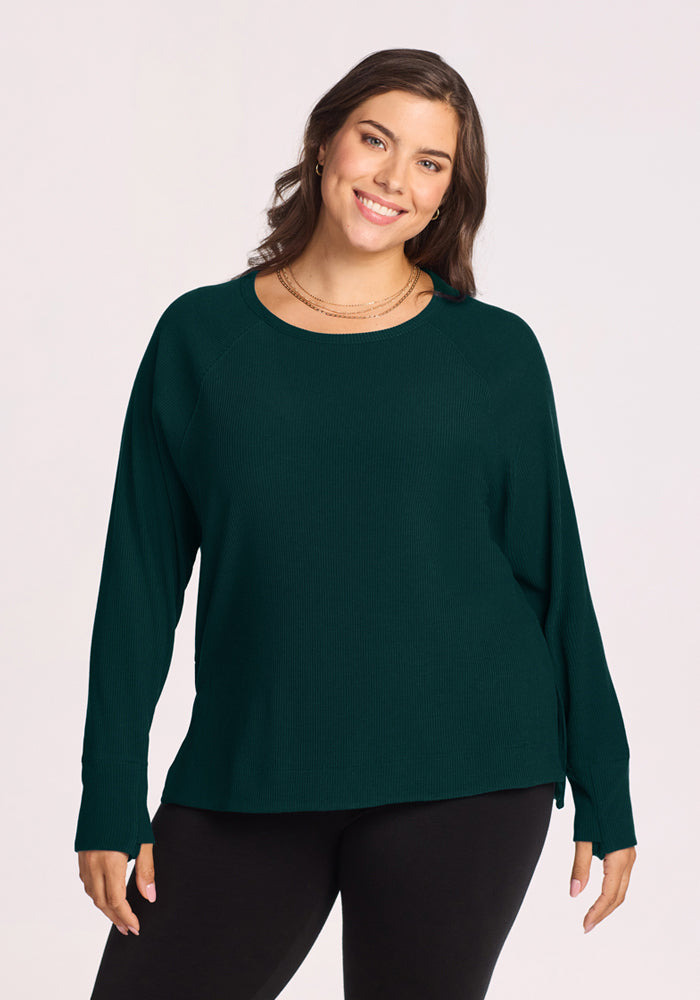 Woman smiling in Woolx Ainsley Sweater - Deep Pine and black pants, against a plain light background. 
