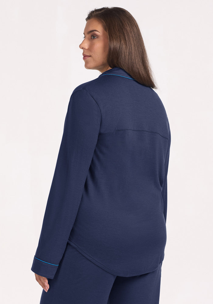 A woman wears the Harper FeatherTouch® Pajama Set - Deep Dive, long-sleeved navy Merino wool pajamas with blue piping.