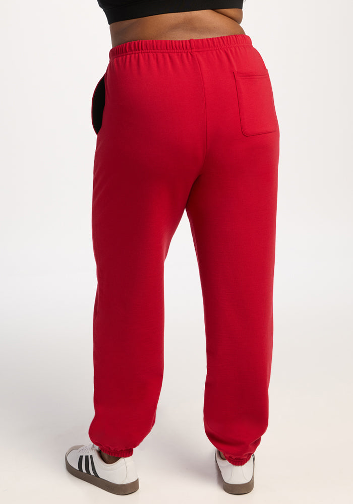 Model in Woolx Juliette Joggers - Maraschino Cherry, white sneakers; back view, plain backdrop.