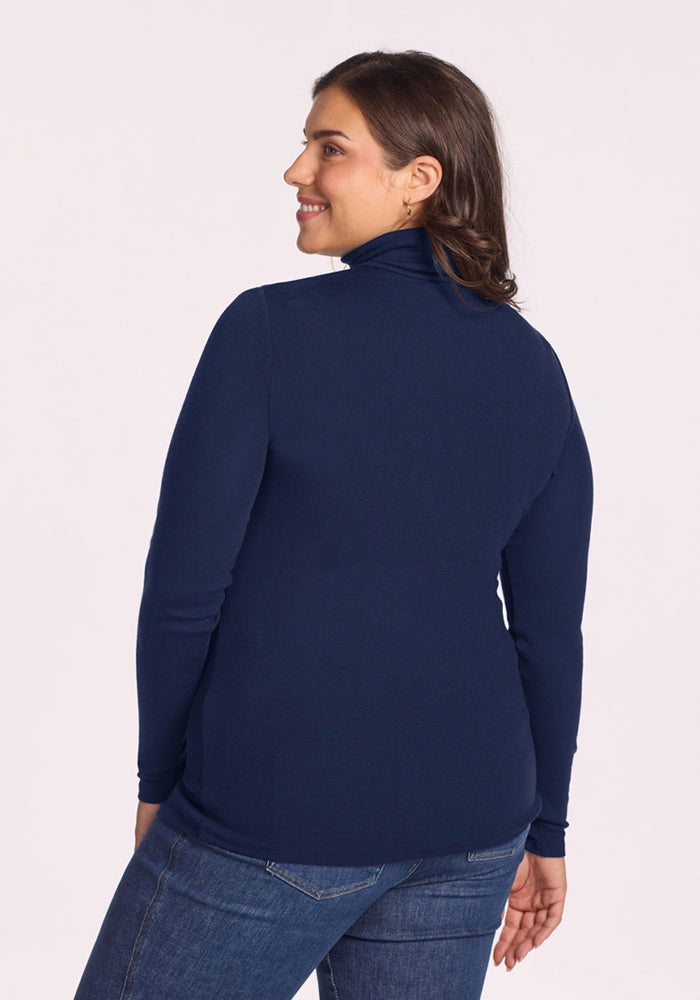 Woman in a Woolx Sage Ribbed Turtleneck - Ocean Cavern and jeans stands with her back to the camera, smiling.