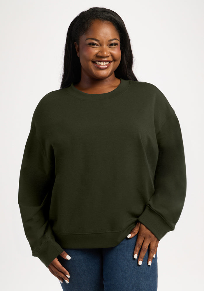 A smiling woman wears a forest green moisture-wicking merino wool Molly Crewneck - Duffel Bag. 
