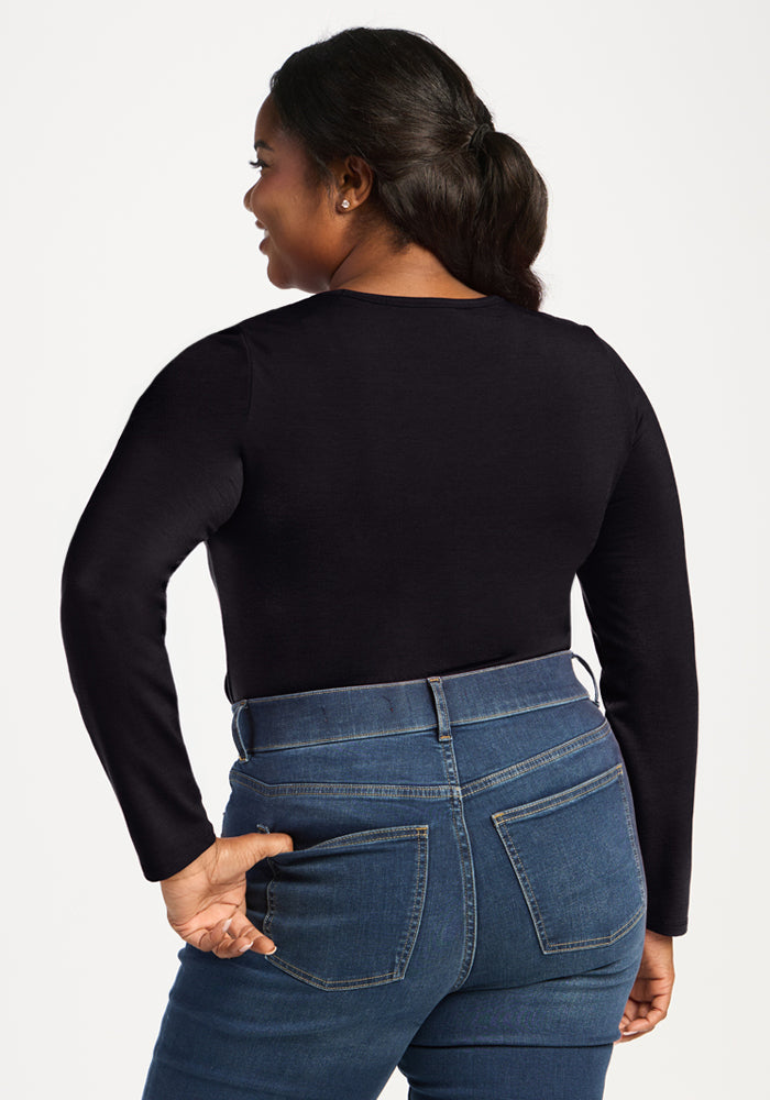 Woman in a Woolx Margot Bodysuit - Black and blue jeans, standing with her back to the camera, smiling.