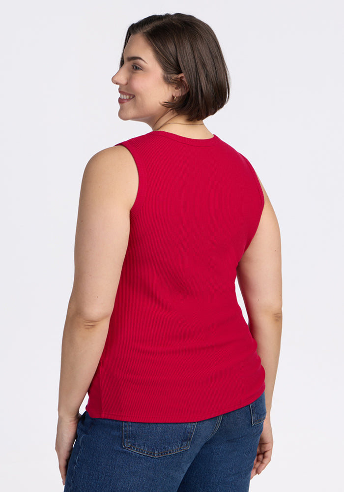 A woman with short brown hair is smiling and facing away from the camera, wearing the Woolx Raegan Ribbed Tank Top in Poppy Spark and blue jeans, standing against a plain white background.