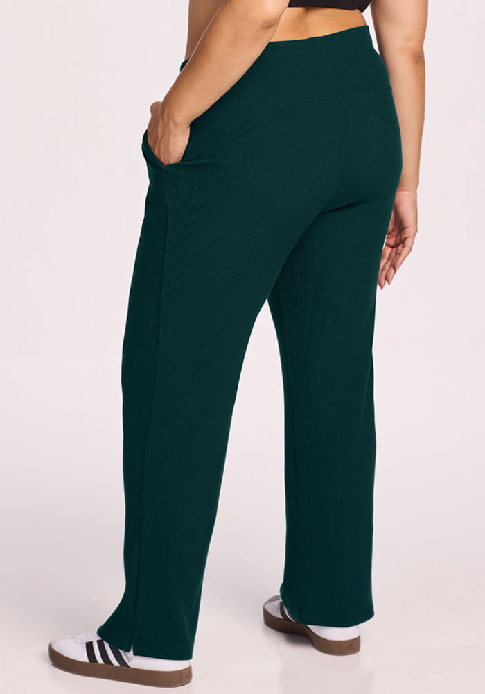 Person in Woolx Luca Ribbed Pants - Deep Pine and white sneakers, shown from the back with one hand in pocket.