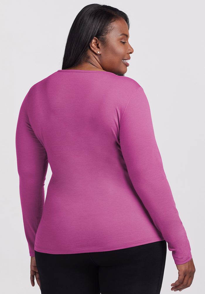 A woman with long dark hair, wearing the Woolx Remi Long Sleeve T-Shirt in Purple Wine and black pants, stands facing away from the camera against a plain light gray background.