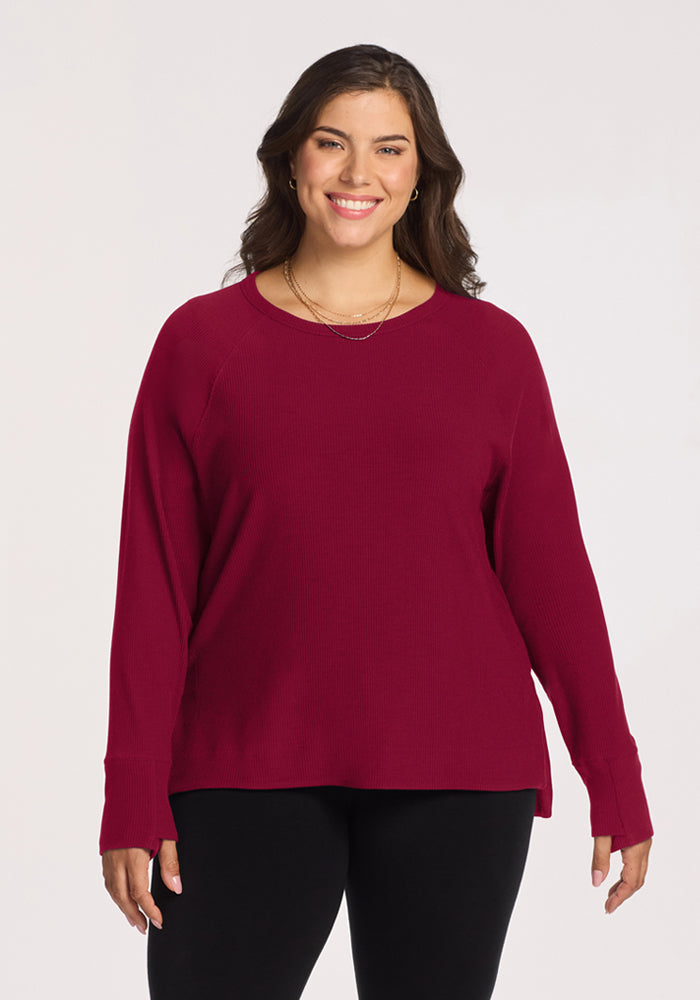 Woman smiles in a Woolx Ainsley Sweater in Beet Red, paired with black pants, against a light background. 
