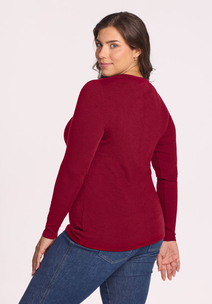 Woman in Woolx Reese Ribbed Henley - Beet Red and jeans stands, looking over her shoulder at the camera.