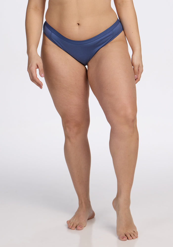A person stands barefoot against a plain background, wearing Woolx Roxie Bikini Underwear in Skyline. The image is cropped from the shoulders down to highlight the torso and legs.