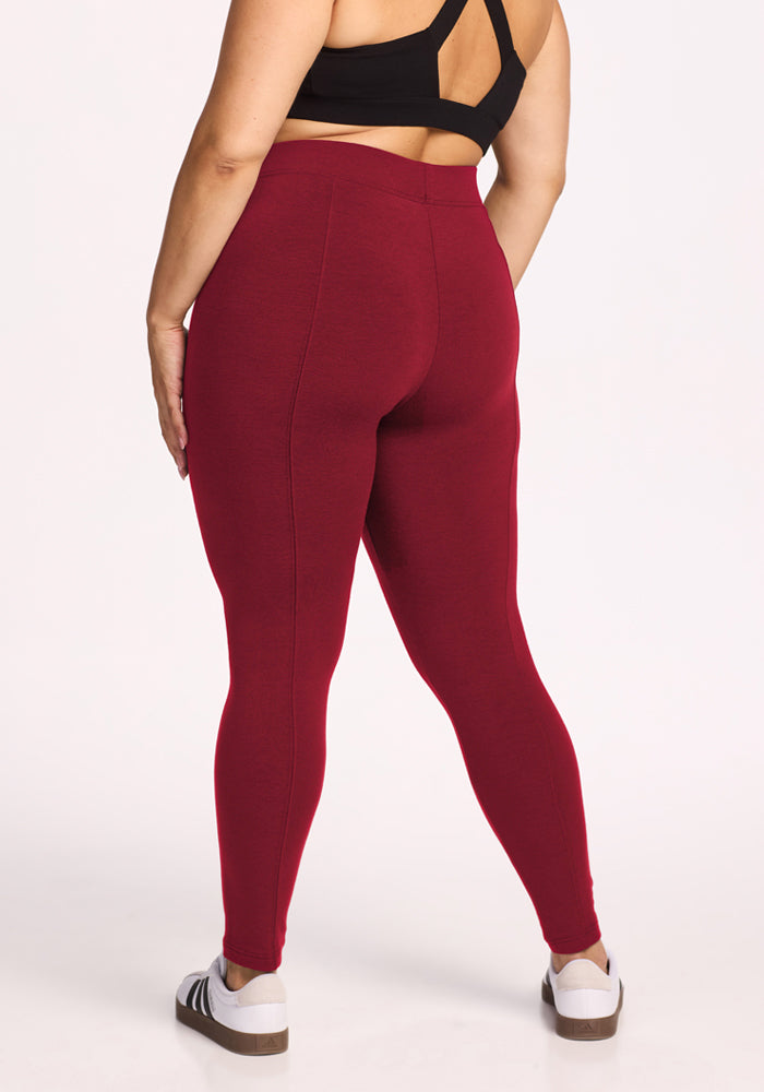 Woman in Woolx Stella Leggings - Pinot Noir, black sports bra, white sneakers, shown from back on white background.