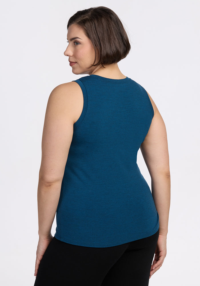 A woman with short brown hair is shown from the back, wearing a sleeveless Woolx Ava Tank Top in Majolica Blue and black pants, standing against a plain white background.