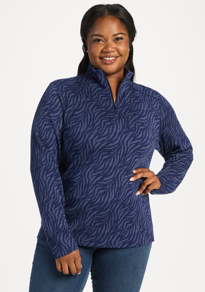 Smiling woman in Woolx Emi 1/4 Zip - Midnight Safari pullover and jeans, posing with a hand on her hip. 