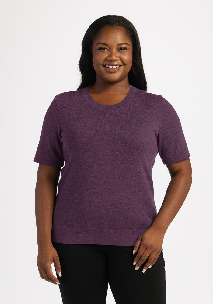 Woman smiling in Woolx Anna Crew Sweater - Purple Iris and black pants, standing against a white background. 