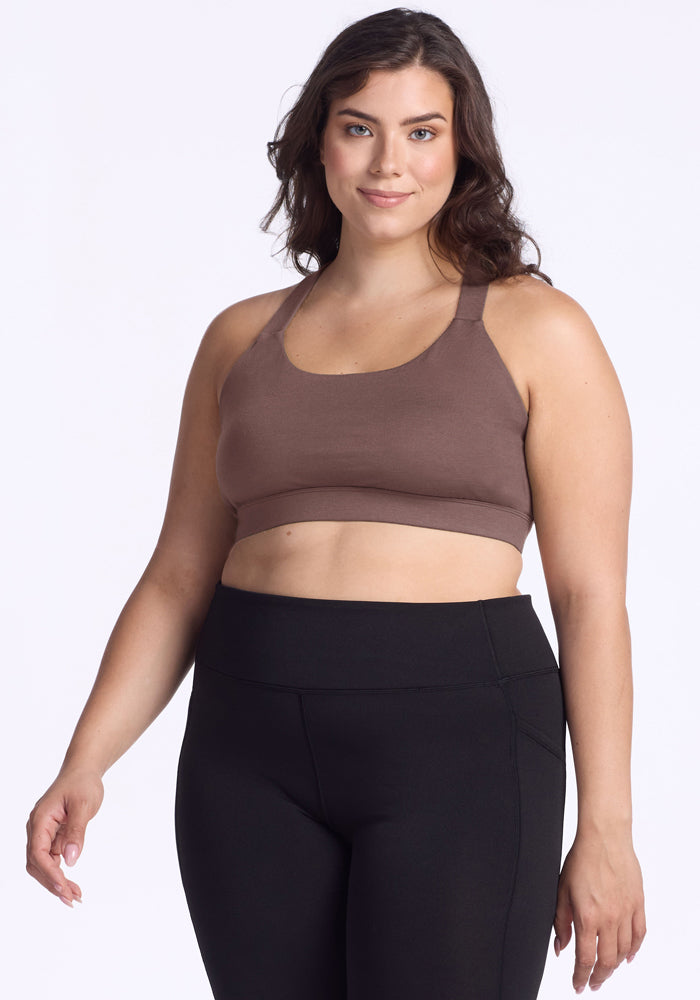 Woman wearing the Woolx Livi Bra in Peppercorn and black leggings, smiling against a plain white background. 