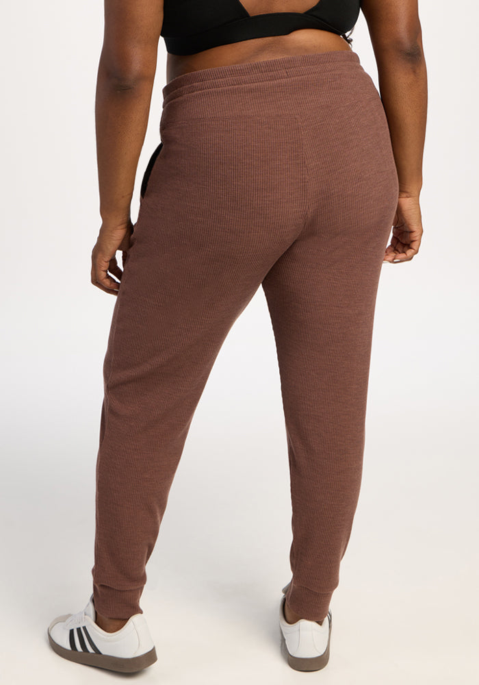Person in Woolx Lennon Ribbed Joggers - Sable Heather, white sneakers with black stripes, and a black top, back view.