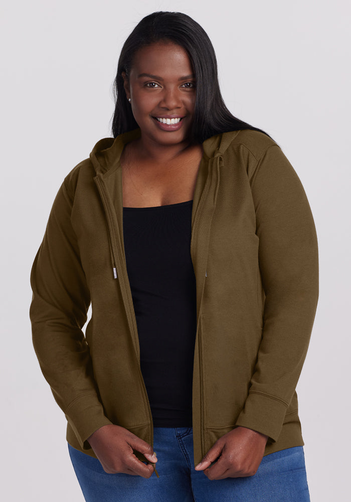 Smiling woman in Woolx Ryann Hoodie - Olive Leaf, black top, blue jeans, posed against a light background. 