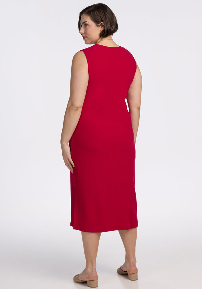 A woman with short brown hair, wearing the Woolx Iris Ribbed Dress in Poppy Spark and beige sandals, stands facing away from the camera against a plain white background.