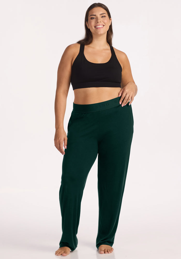 A smiling person wearing a black sports bra and Deep Pine Maya Lounge Pants with an elastic waistband.