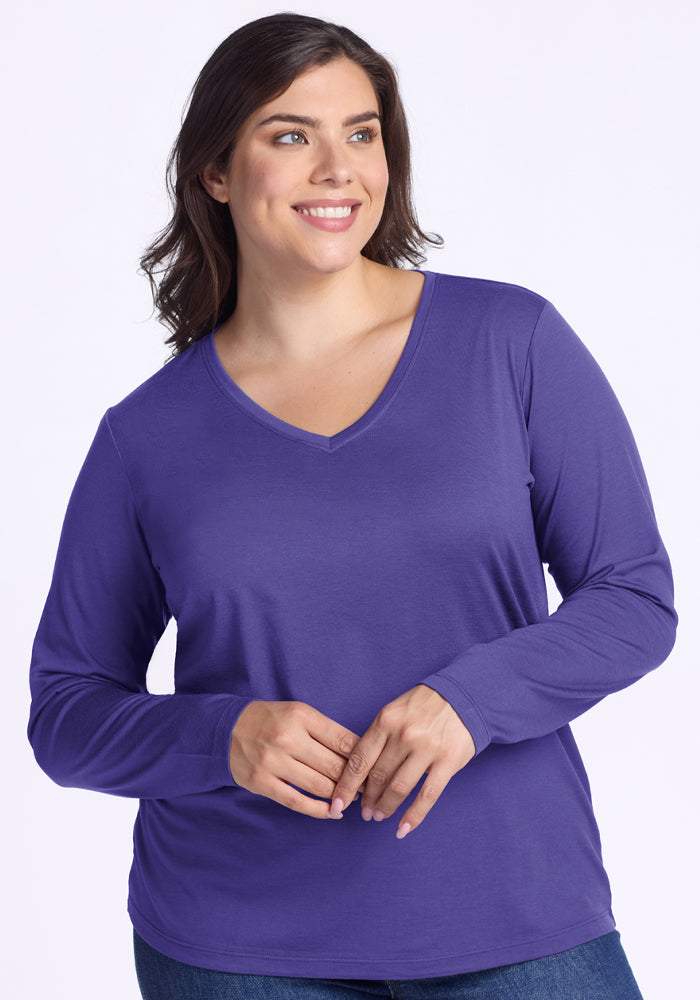 Smiling woman in Woolx Millie Long Sleeve - Berry Indigo and jeans stands against a plain light background. 