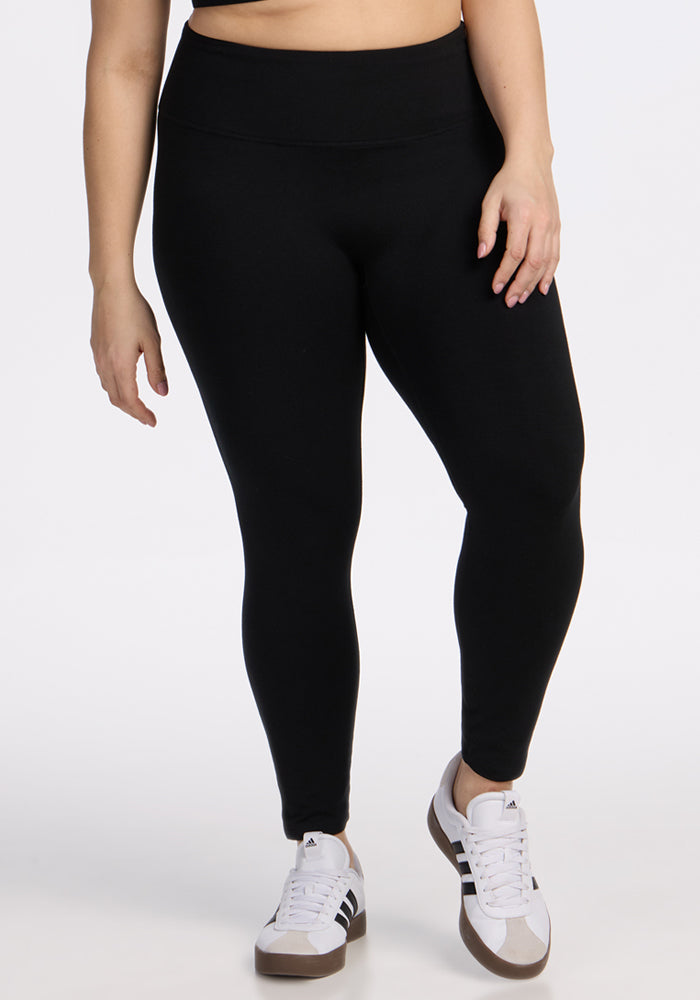 A person wearing Woolx Angela Leggings - Black and white sneakers with black stripes stands against a plain white background. Only the lower half of the body is visible. 