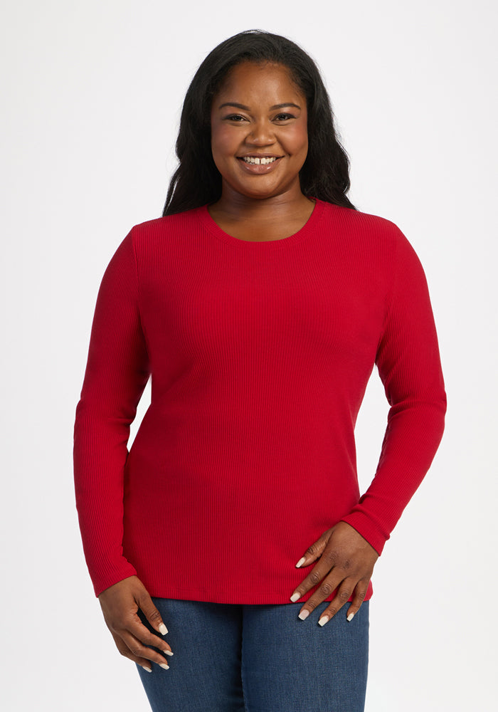 Smiling woman in Woolx Hadley Ribbed Crew - Maraschino Cherry and blue jeans, standing against a white background. 