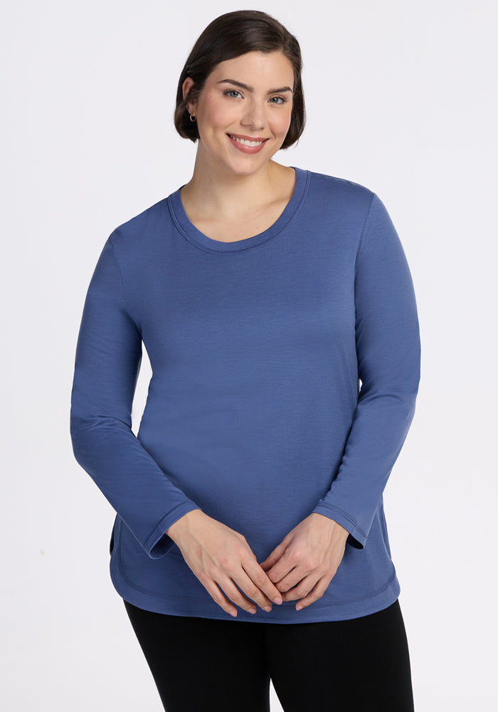 A woman with short brown hair smiles while wearing the Woolx Hazel Tunic - Skyline and black pants, standing against a plain white background. 