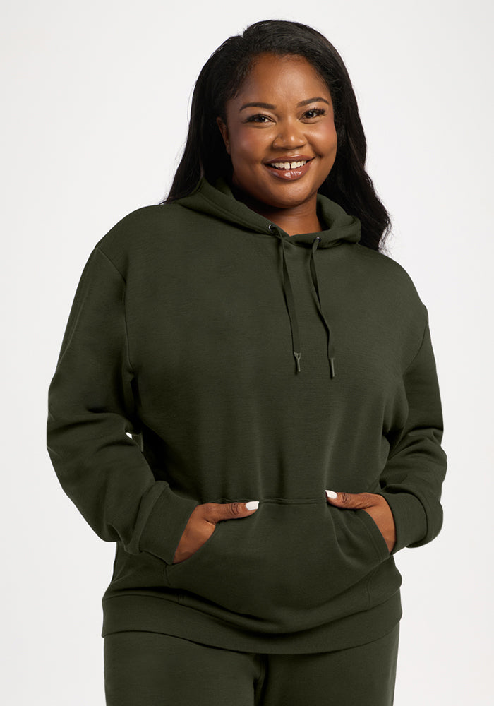 Woman wearing the Woolx Avery Hoodie - Duffel Bag, hands in front pocket, standing against a white background. 
