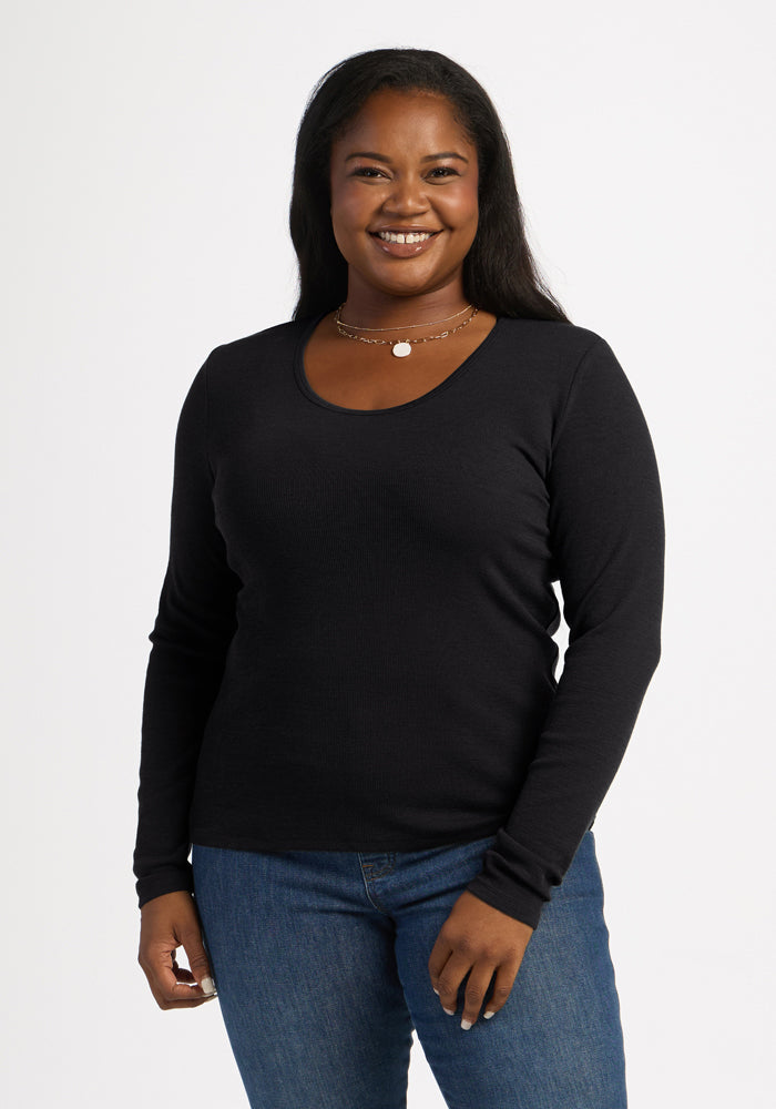 Woman smiles in Woolx Katie Ribbed Long Sleeve - Black, paired with blue jeans, against a white background. 