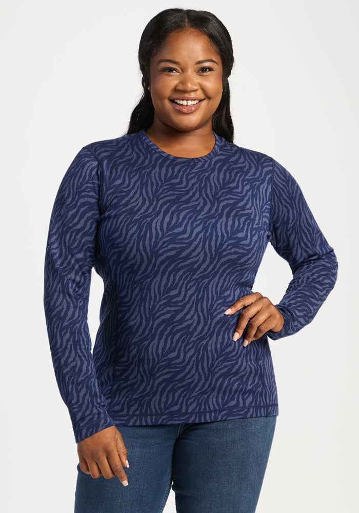 Smiling woman in Woolx Maddie Baselayer Top - Midnight Safari and jeans, confidently posing with a hand on her hip. 