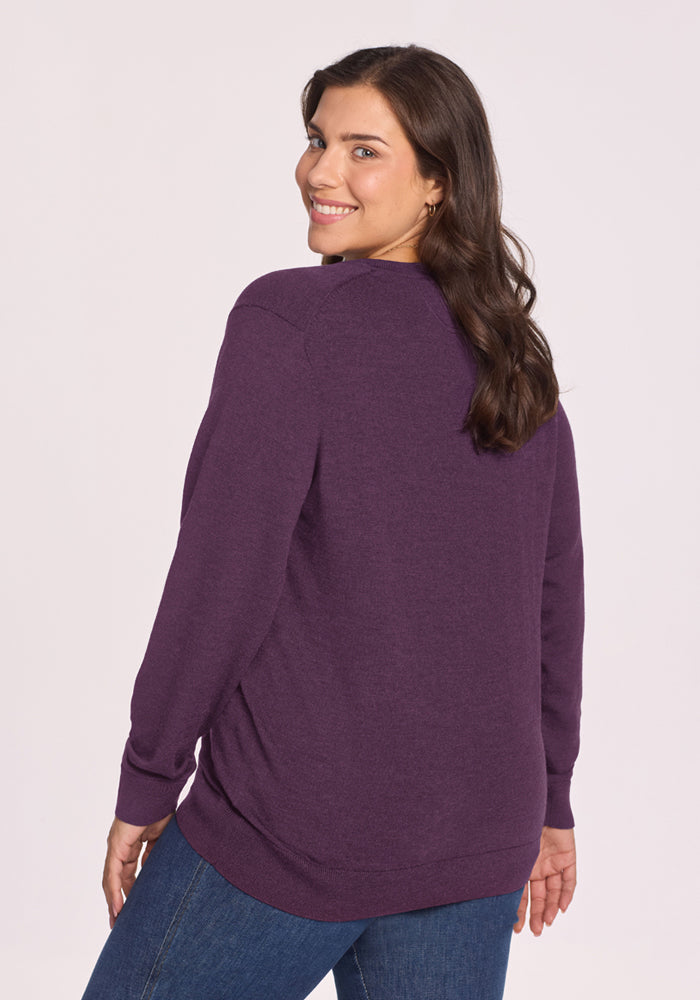 Woman wearing Woolx Francesca Sweater in Purple Iris and blue jeans, smiling, looking over her shoulder at the camera.