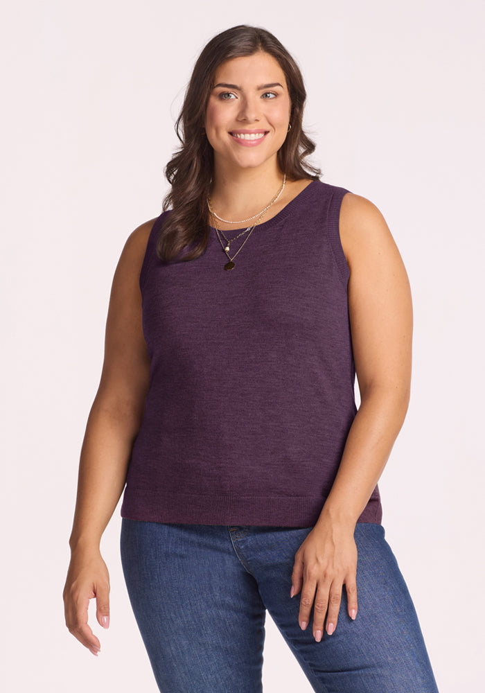 Smiling woman in Woolx Chessy Tank Top - Purple Iris and jeans, with wavy brown hair, on a light background. 