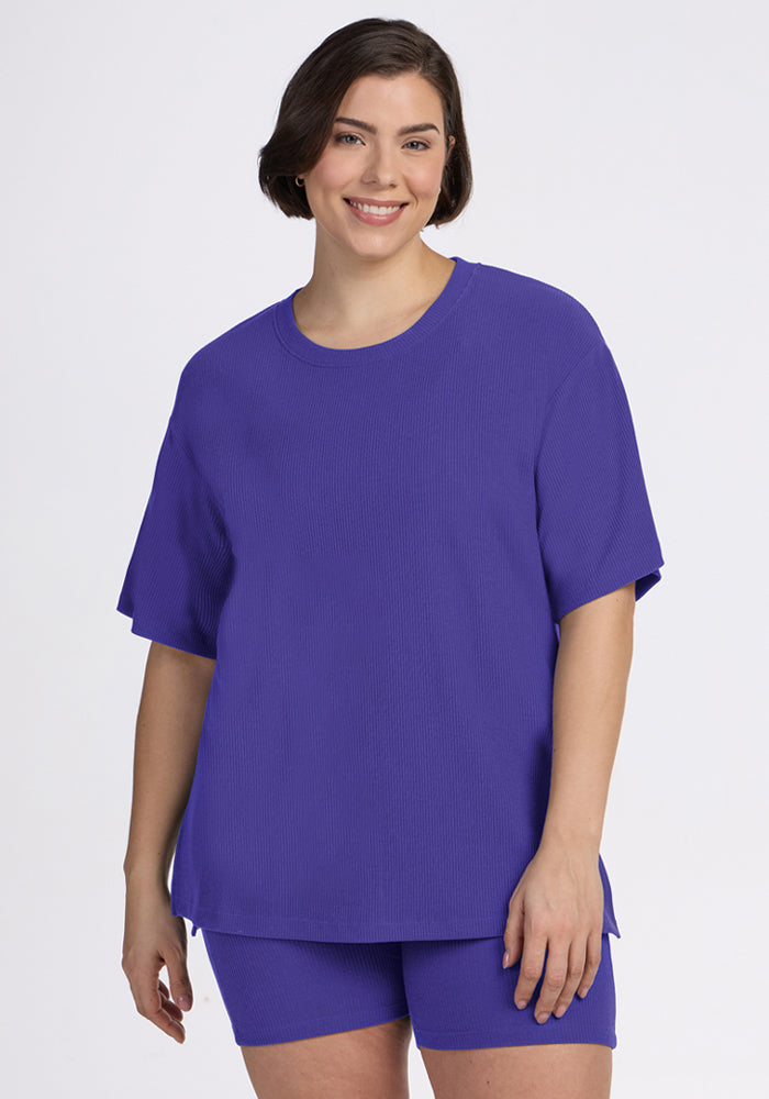 A woman smiles in the Woolx Vera Ribbed Tunic in Berry Indigo with matching shorts against a plain light background. 
