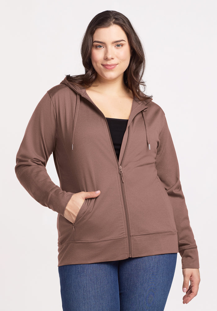 Woman in a Woolx Ryann Hoodie in Toasted Almond and blue jeans, smiling with one hand pocketed—a travel essential. 