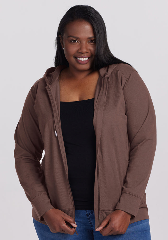 Woman smiling, wearing the Woolx Ryann Hoodie in Peppercorn over a black top and blue jeans—a true travel essential. 