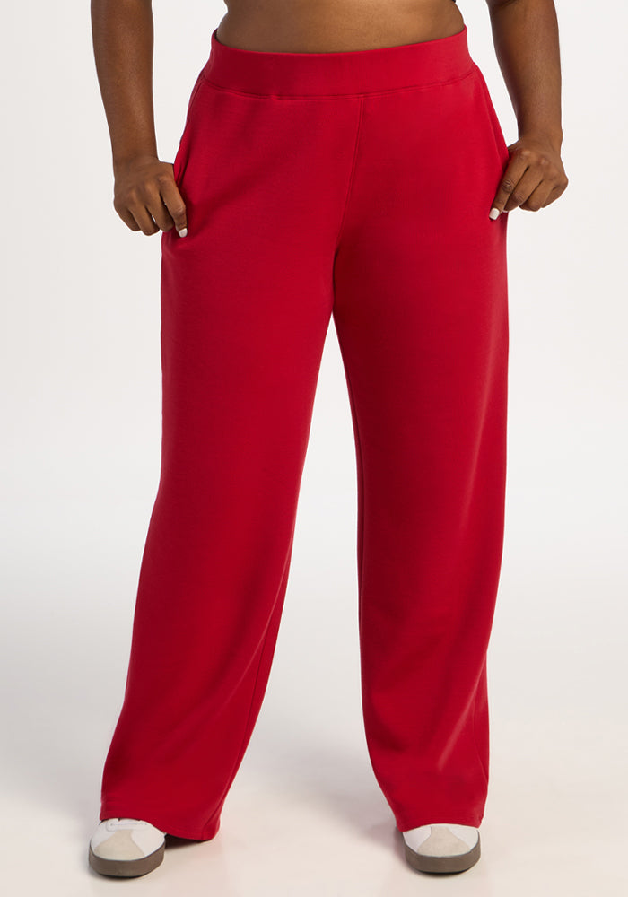 Model wears Woolx Bree Lounge Pants in Maraschino Cherry with white shoes, hands in pockets, on a plain background. 