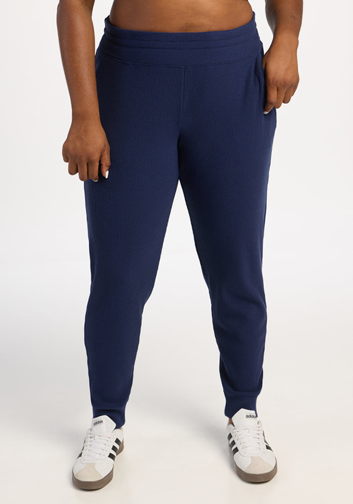 Model in Woolx Lennon Ribbed Joggers - Ocean Cavern with white sneakers, standing against a plain white background. 