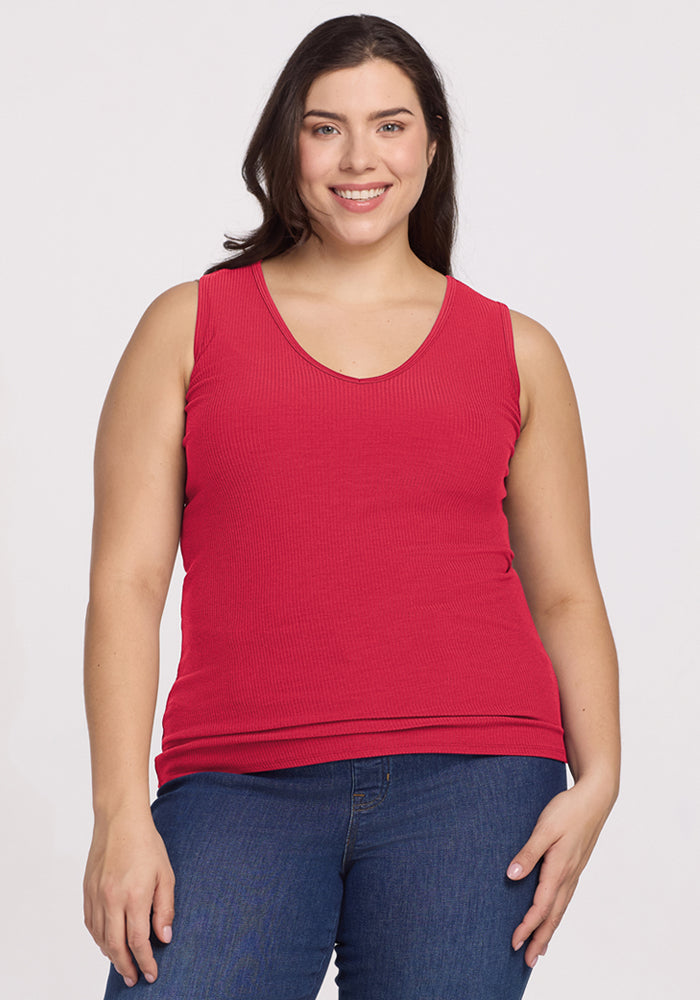 Smiling woman wears the Woolx Vivi Ribbed Tank in Berry Ice Pop and blue jeans against a plain light background. 