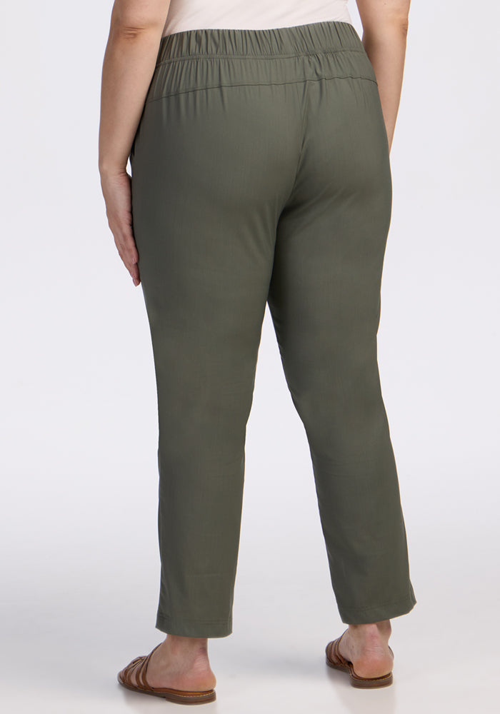 A person is shown from the back, wearing Woolx Nicole Ankle Pants in Sage Olive and brown sandals, standing against a plain white background.