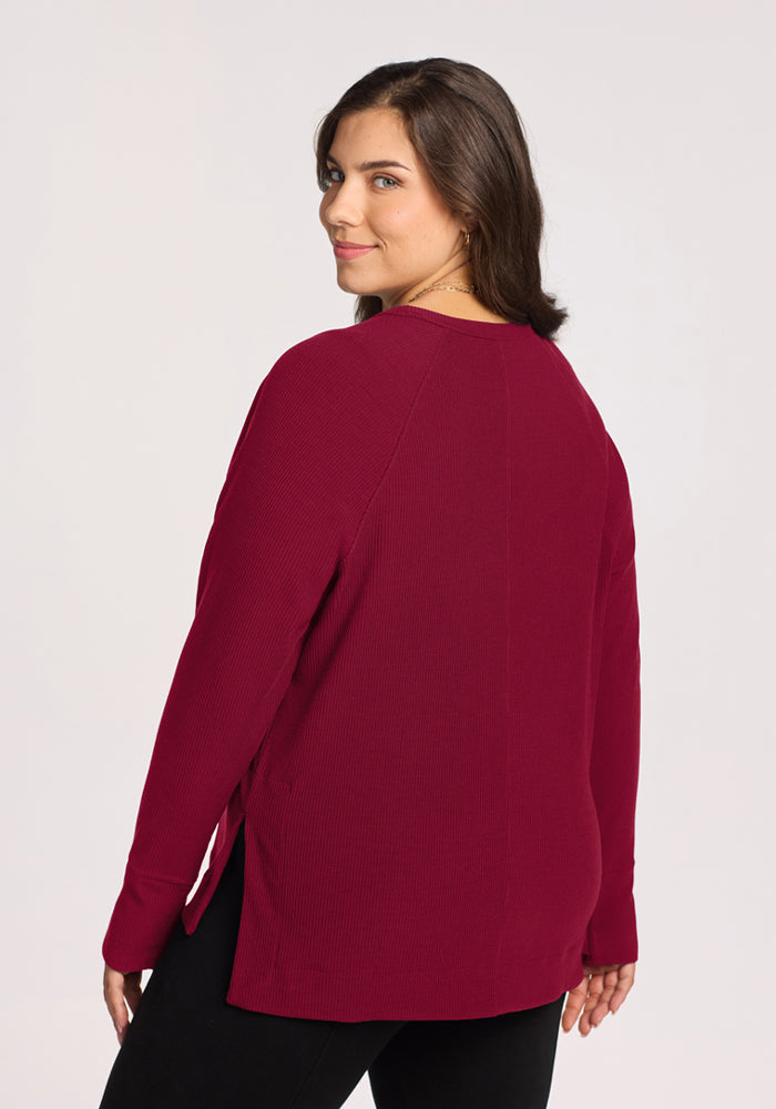 Woman in the Woolx Ainsley Sweater in Beet Red and black pants looks back, her wavy brown hair flowing.