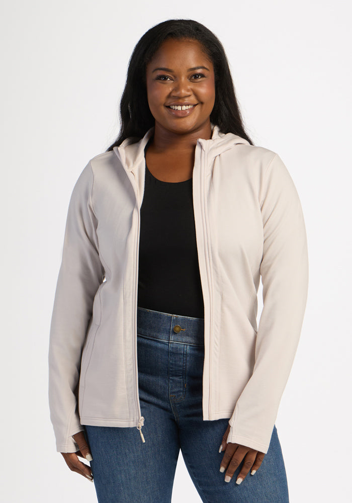Woman in a Woolx Zoey Zip Up Hoodie in Ecru, black top, and blue jeans, standing and smiling at the camera. 