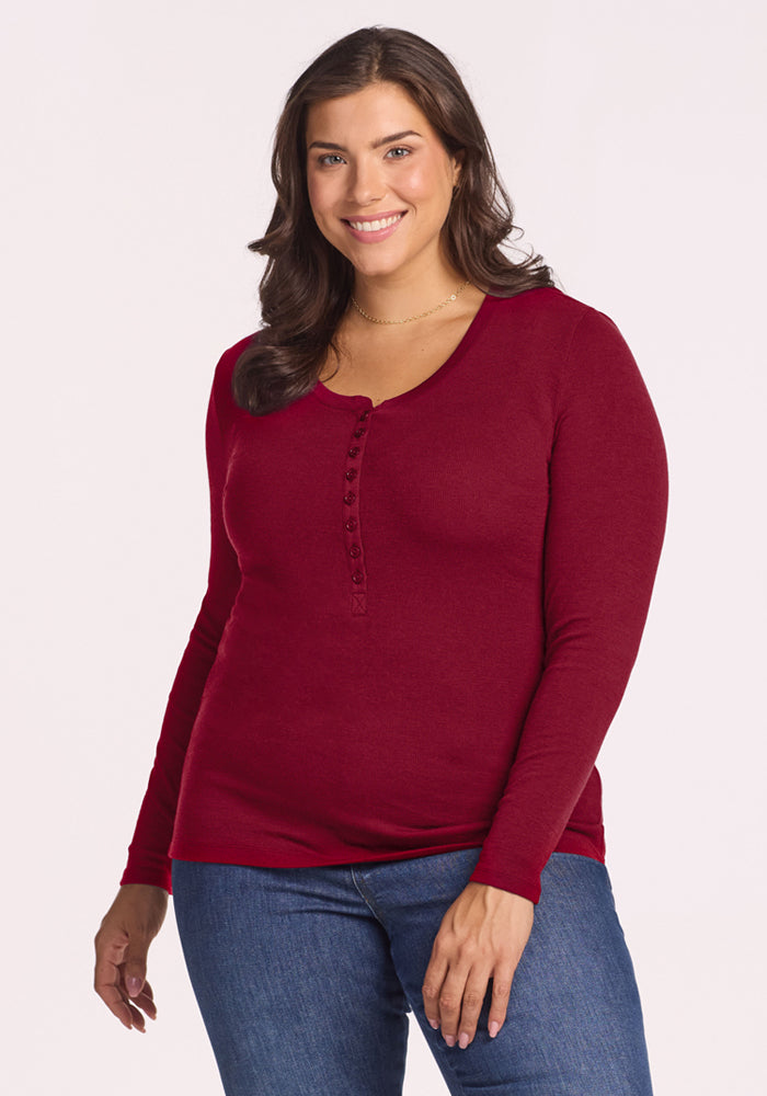 Woman in the Woolx Reese Ribbed Henley - Beet Red and blue jeans smiles at the camera against a plain background. 