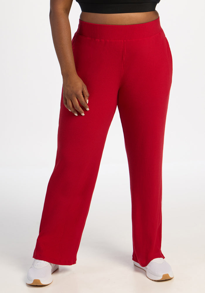 Model wears Woolx Luca Ribbed Pants in Maraschino Cherry, white sneakers, and a black crop top against a white background. 