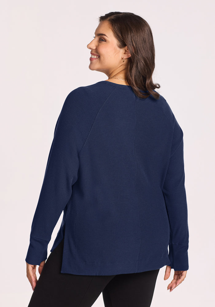 Smiling woman in Woolx Ainsley Sweater—Ocean Cavern, with black pants, turned to show the back of her outfit.