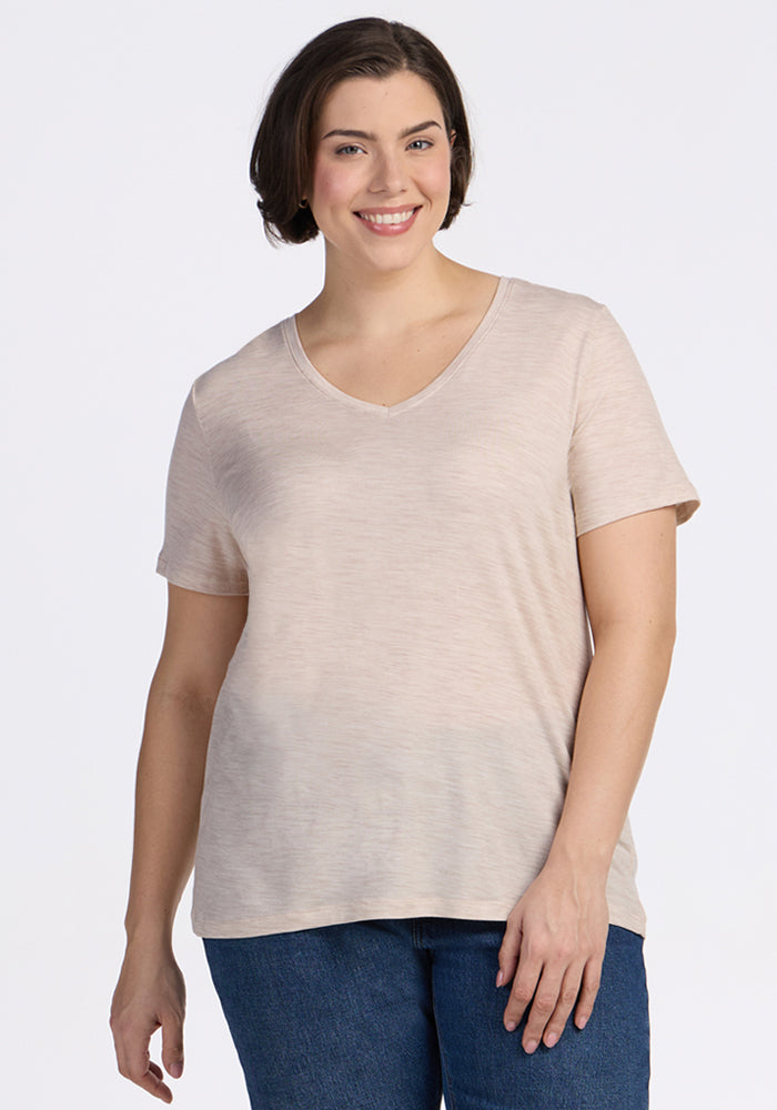 A woman with short dark hair smiles while wearing the Woolx Junie V Neck in Cream Heather and blue jeans, standing against a plain white background. 