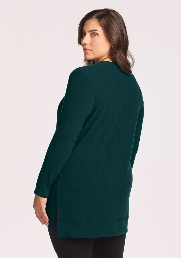 A woman with brown hair models the Woolx Evie Ribbed Tunic in Deep Pine, shown from the back on a light background.