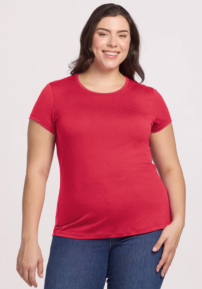 Woman smiles in a Woolx Addie Crew Neck - Berry Ice Pop Merino T-shirt and blue jeans against a plain background. 