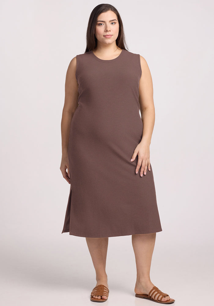 A woman wears the Woolx Iris Ribbed Dress in Peppercorn and sandals, standing against a light background. 