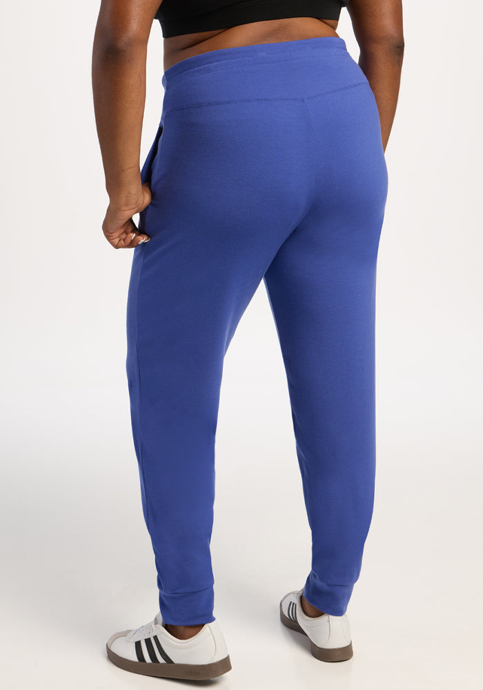 Model wears Woolx Madden Joggers in Royal Blue, black crop top, and white sneakers; back view on white background.
