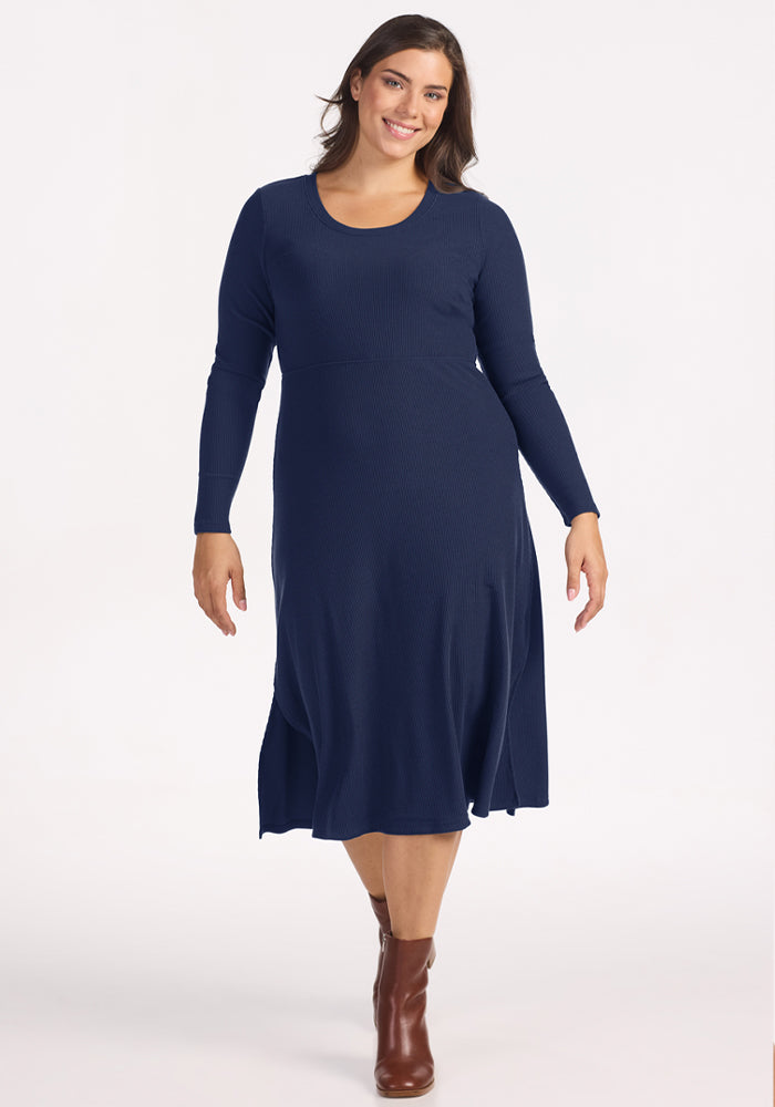 Woman in Woolx Caroline Ribbed Twirl Dress - Ocean Cavern and brown ankle boots stands against a white background. 