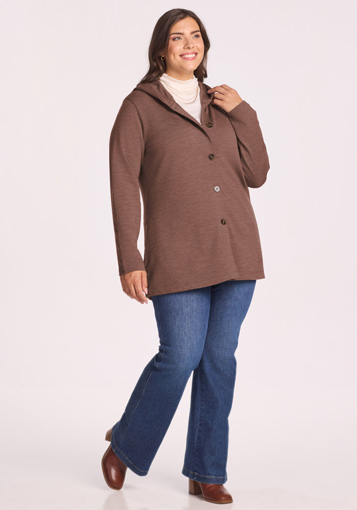 Woman in Woolx Edna Hooded Cardigan - Sable Heather, blue jeans & brown boots, smiling against light background.
