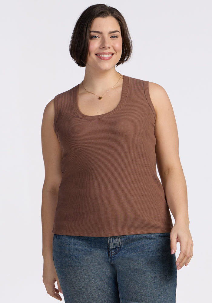A woman with short brown hair smiles while wearing the Woolx Sloane Ribbed Tank in Sienna Kiss and blue jeans, standing against a plain white background. 